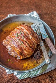 a piece of meat is in a pan with sauce and a fork on the side