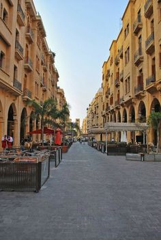 an empty city street lined with buildings and tables on either side of the road,