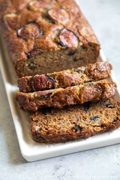 two slices of banana bread on a white plate next to another loaf of fruit bread