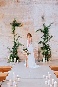 a woman standing in front of a brick wall with candles and greenery around her