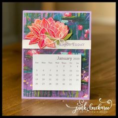 a calendar card with a flower on it sitting on a wooden table in front of a window