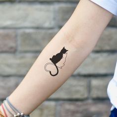 a black cat tattoo on the arm of a woman's left arm, with a brick wall in the background