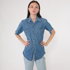 Vintage 90s Wrangler shirt in blue denim with pearl snaps down the front and a Western yoke. It has short cutoff sleeves and chest pockets.  Please see measurements and condition below. Every garment we sell is authentic vintage and one-of-a-kind! You will receive the exact item photographed. Condition:  Lightly distressed. Sleeves are cutoff and frayed, hem is also frayed. Has a few runs on the sleeve. Size label: Labelled 14 1/2 - 33 regular fit x-long tails Best fits: men's small, women's Medium Tag: Wrangler Material: Feels like Cotton Era: 90s MEASUREMENTS Taken from seam to seam while the garment is lying flat. Double the armpit, waist, and hips For reference, model is 5'7" and measures 31-24-34. Length from Top: 27" Armpit to Armpit: 19.5" Waist: 17.5" Shoulder to Shoulder: 15.5" Sl Levi's Button-up Tops, Wrangler Denim Shirt, 1990s Men, Wrangler Shirt, Wrangler Vintage, Cowboy Rodeo, Western Jeans, Jean Shirt, Wrangler Shirts