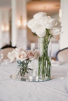 two vases with white flowers on a table in front of some wineglasses