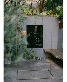 a black and gold wedding sign with greenery in the background