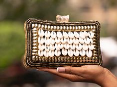 Enriched with the affirming symbol of wealth, our the Mozwi Evening Clutch is a beautiful and exclusive accessory. Crafted from cowrie shells, beads, and a detachable chain, this purse adds an enigmatic and lavish sophistication to any outfit. -measures: 8 x 5 inches -material: cowrie, beeds, threading, metal -handmade -imported Bohemian Beaded Gold Clutch, Bohemian Gold Beaded Clutch, Elegant Embellished Beach Bag, Elegant Embellished Beach Bags, Handmade Bohemian Gold Clutch, Bohemian Handmade Gold Clutch, Elegant Beach Clutch, Elegant White Clutch For Beach, Elegant White Beach Clutch