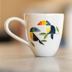 a coffee cup with colorful birds painted on it's side sitting on a table