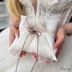 a woman is holding a white wedding ring pillow