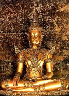 a golden buddha statue sitting on top of a wooden table in front of a brick wall