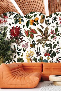 an orange leather couch sitting in front of a wall with flowers and leaves on it