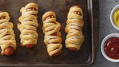 four hotdogs wrapped in bread with ketchup and mustard on a baking sheet