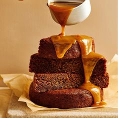 a person pouring caramel sauce on top of a piece of cake with two slices stacked on each other