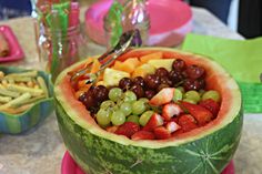 a watermelon filled with grapes, strawberries and kiwis is sitting on a table