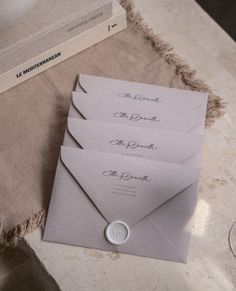 three envelopes are sitting on a table next to some wine glasses and a book