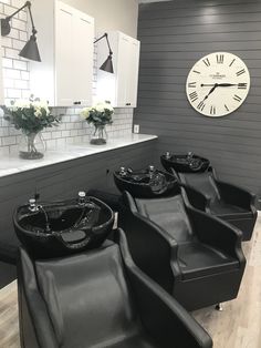 a salon with black chairs and a large clock on the wall above it's windows