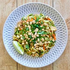 a white bowl filled with noodles and veggies on top of a wooden table