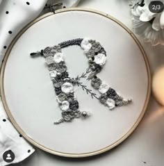 an embroidered monogram with flowers and beads is displayed on a white tablecloth next to a lit candle