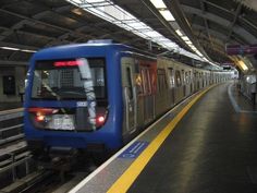 a blue train traveling down tracks next to a loading platform