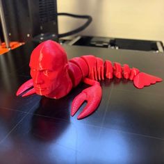 a red plastic lobster sitting on top of a table next to a black computer monitor