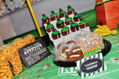 a football themed dessert table with snacks and candies on the trays in front of it