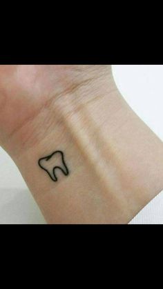 a small black tooth tattoo on the left side of the wrist, with an outline of a tooth