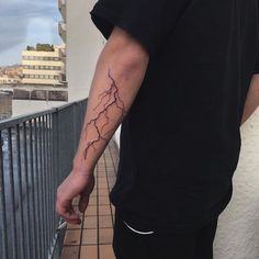 a man with a lightning tattoo on his arm holding onto a cell phone while standing next to a fence