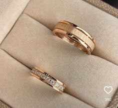 two gold wedding rings sitting on top of a velvet cushioned box with diamond accents