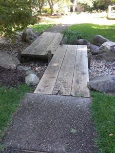 a wooden bench sitting on top of a grass covered field next to rocks and trees