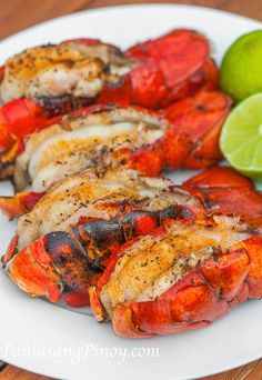 grilled lobsters on a white plate with lime wedges and red pepper sauce