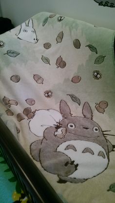 a bed with a totoro blanket on it's side and an animal pillow behind it