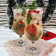 two glasses filled with fruit and ice sitting on top of a table next to a christmas tree