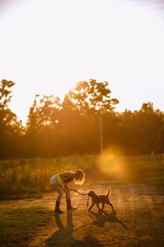 a woman walking her dog on a dirt road in the evening sun with trees and grass behind her