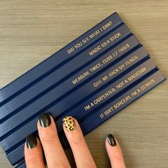 a woman's hand with black and gold nail polish next to four blue pencils