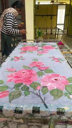 a woman standing next to a table with flowers painted on it and another person in the background