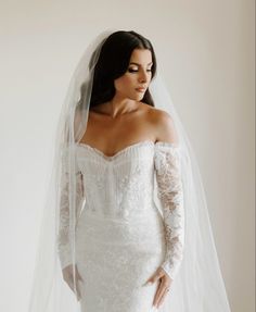 a woman in a white wedding dress with a veil on her head and one arm over her shoulder