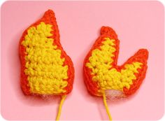 two crocheted orange and yellow mittens sitting on top of a pink surface