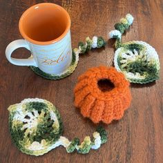 a crocheted coffee cup cozying next to an orange and green mug coziet