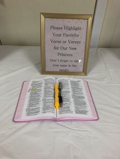 an open book with a pen sitting on top of it next to a sign that says please highlight your favorite verse or verses for our new princess