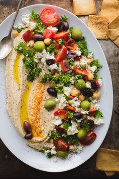 a white plate topped with food next to a bowl of olives and tomatoes