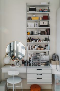 a white desk topped with lots of drawers next to a mirror and shelf filled with cosmetics