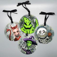 three halloween ornaments hanging from black ribbons on a white surface with an image of skeletons and witches