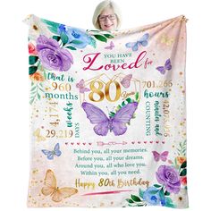 a woman holding up a birthday blanket with butterflies and flowers on it that says, you have loved the 80th anniversary