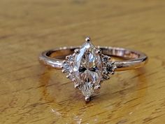 an engagement ring with a pear shaped diamond surrounded by smaller diamonds on a wooden surface