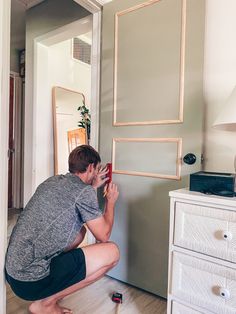 a man kneeling on the floor in front of a mirror taking a photo with his cell phone