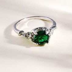 a close up of a ring with a green stone in it on a white surface