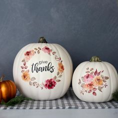 two white pumpkins with painted flowers and give thanks written on the front, sitting next to each other