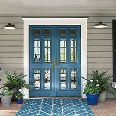 a blue front door with two potted plants on the side and an area rug