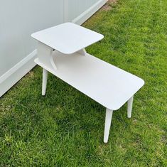 a white table sitting in the grass next to a wall and fenced in area