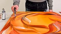 a man is painting an orange and brown design on a piece of art with acrylic paint