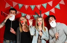 four people are posing for a photo in front of a red wall with christmas decorations